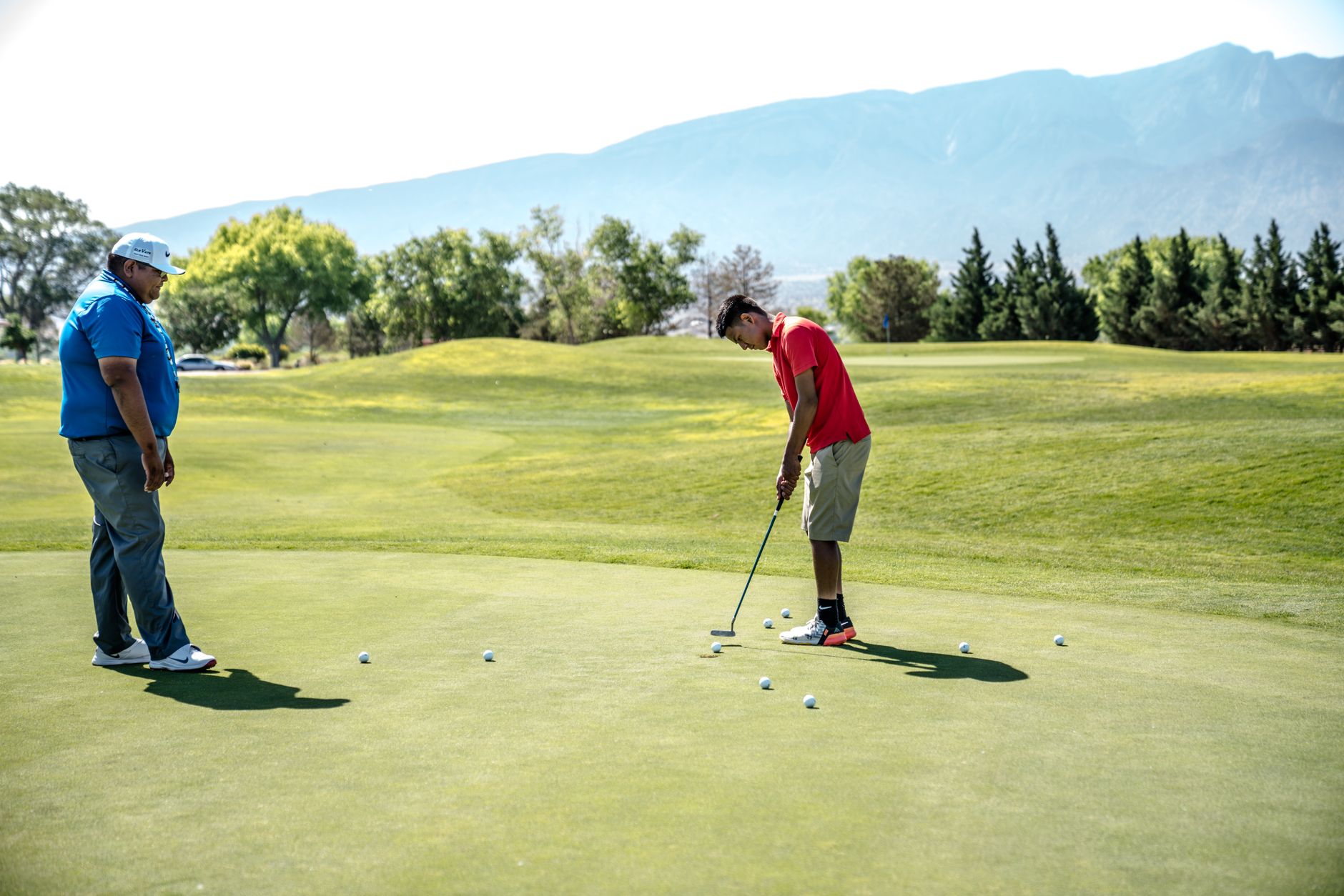 Two men practicing putting on a sunny golf course with mountain views. — photograph by Jopwell on Pexels