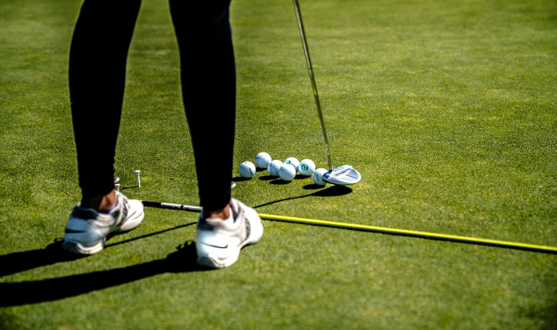 A golfer practicing putting on a sunny day with several golf balls on the green. — photograph by Jopwell on Pexels