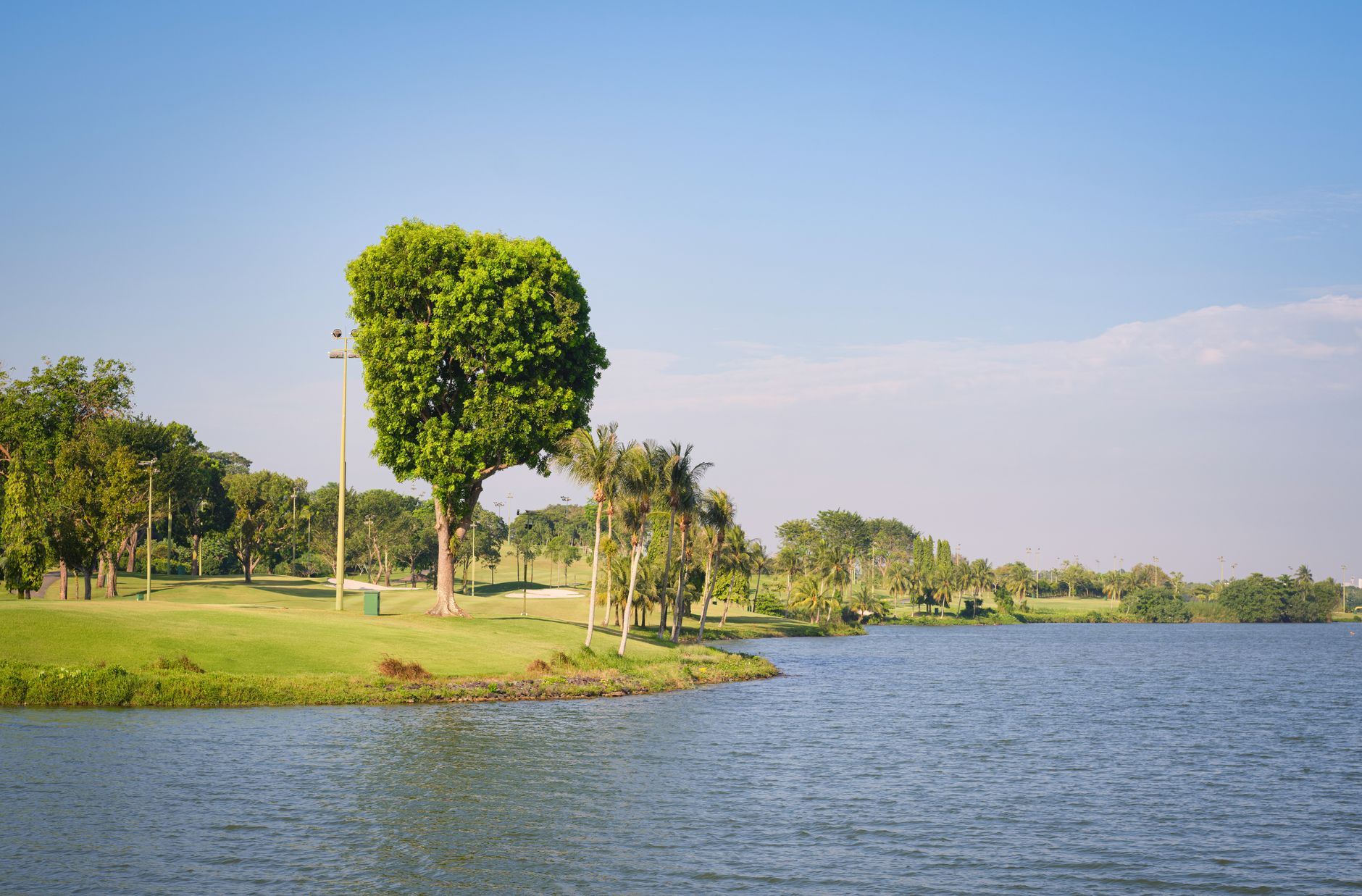 Beautiful view of a green golf course and lake under a bright blue sky, evoking tranquility and leisure. — photograph by Calvin Seng on Pexels